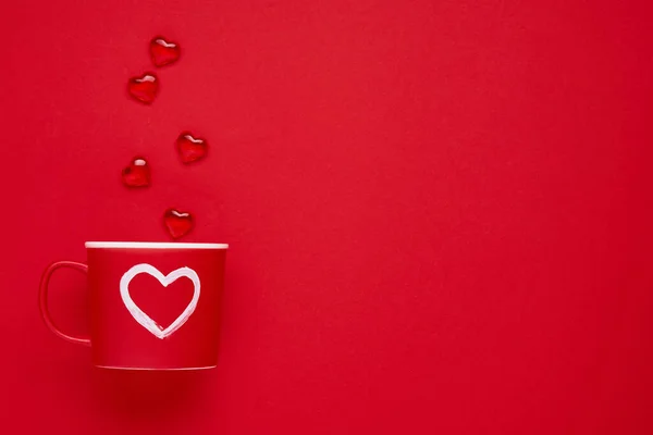 Red cup mug with with painted heart, sugar and chocolate hearts on scarlet or red background. Flat lay composition. Valentines Day concept. Top view, copy space.