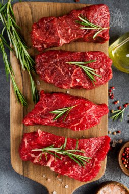Baharatlı, soğanlı ve biberiyeli çiğ biftek. Koyu levha ya da beton arka plan. Üst görünüm