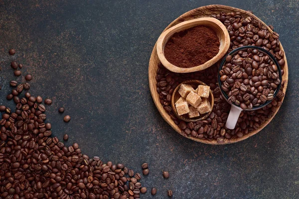 stock image Coffee roasted beans in cup and scattered nearby, ground coffee and cane sugar on a brown table background. Top view with space to copy text.