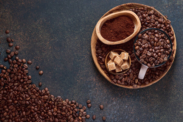 Coffee roasted beans in cup and scattered nearby, ground coffee and cane sugar on a brown table background. Top view with space to copy text.