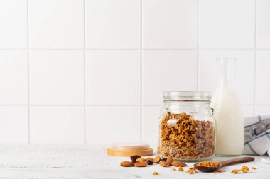 Bir şişe süt, fındık ve kuru meyveli yulaf ezmesi, parlak bir mutfak masasında sağlıklı bir kahvaltı hazırlamak için seramik kaseler. İskandinav beyaz tarzı. Seçici odak.