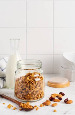 Bir şişe süt, fındık ve kuru meyveli yulaf ezmesi, parlak bir mutfak masasında sağlıklı bir kahvaltı hazırlamak için seramik kaseler. İskandinav beyaz tarzı. Seçici odak.