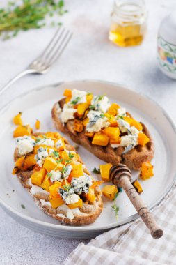 Fırınlanmış balkabağı sandviçi, mavi küflü Dorblu peynirli, bal ve kekik, beton, eski, aydınlık arka planda. Üst görünüm.