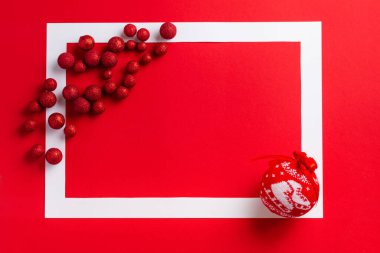 Noel şenliği geçmişi. Kırmızı arka planda kırmızı Noel süslemeleri olan beyaz çerçeve. Mesaj için yer. Üst görünüm.