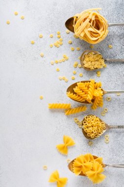 Demir kaşıklarda çeşitli makarnalar ve gri beton arka plan. Anellini makarnası. Yemek pişirme konsepti. Üst görünüm.