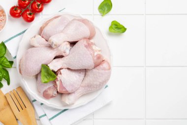 Çiğ tavuk bacağı, domates vişneli, otlu, fesleğenli ve baharatlı, beyaz mermer arka planda, uzay manzarasını kopyala. Sağlıklı beslenme öğle yemeği konsepti.