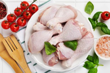 Çiğ tavuk bacağı, domates vişneli, otlu, fesleğenli ve baharatlı, beyaz mermer arka planda, uzay manzarasını kopyala. Sağlıklı beslenme öğle yemeği konsepti.