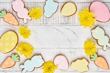 Paskalya tebrik kartı içinde renkli tavşanlar, yumurtalar, tavuklar ve havuçlu kurabiyeler olan beyaz ahşap arka planda fotokopi alanı olan zencefilli kurabiyeler. Model yap. Pankart. Üst görünüm.