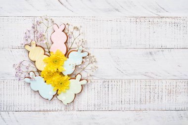 Paskalya tebrik kartı içinde renkli tavşanlar, yumurtalar, tavuklar ve havuçlu kurabiyeler olan beyaz ahşap arka planda fotokopi alanı olan zencefilli kurabiyeler. Model yap. Pankart. Üst görünüm.