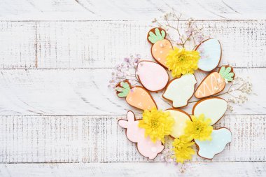 Paskalya tebrik kartı içinde renkli tavşanlar, yumurtalar, tavuklar ve havuçlu kurabiyeler olan beyaz ahşap arka planda fotokopi alanı olan zencefilli kurabiyeler. Model yap. Pankart. Üst görünüm.