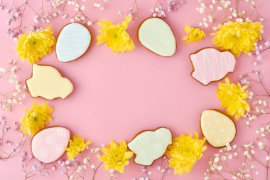 Renkli tavşanların, yumurtaların, tavukların, havuçların, zencefilli kurabiyelerin ve pembe arkaplanlı sarı kasımpatı çiçeklerinin olduğu Paskalya tebrik kartı. Model yap. Pankart. Üst görünüm.