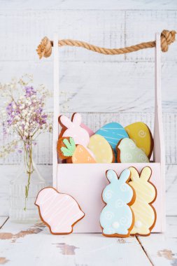 Ahşap duvarın önünde renkli tavşanlar, yumurtalar, tavuklar ve havuçlu kurabiye sepeti olan Paskalya tebrik kartı. Model yap. Üst görünüm.