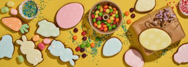 Paskalya pişirme geçmişi. Çok renkli Paskalya zencefilli ekmek, şeker, dağınık şekerleme sosu ve sarı arka planda hediye kutusu. Kutlama geçmişi konsepti. Pankart. Metin için boşluk.