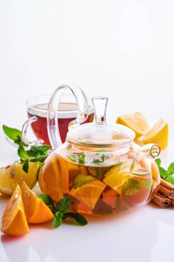 Beyaz arka planda limon, portakal, nane ve tarçın dilimli çaydanlıkta çay..