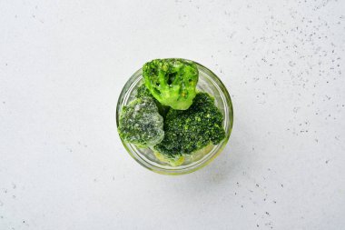 Donmuş sebzeler, cam kaselerde buzun üstünde yeşil brokoli ve fotokopi alanı olan beton gri arka plan..