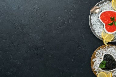 Kalp şeklinde kırmızı ve siyah havyar. Siyah arka plan masasında limon ve buz küpleriyle servis ediliyor. Metin için boşluk.