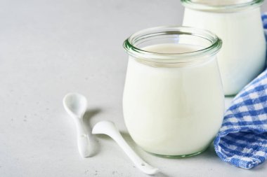 Açık gri arkaplan üzerine kaşık, sağlık ve diyet konsepti içeren cam bir kavanozda ekşi krema veya doğal yoğurt.