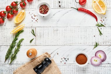 Baharatlı Pişirme Arkaplanı: biber, biberiye, paprika, limon, soğan, kuşkonmaz, zeytinyağı, domates, parmesan peyniri, ahşap zemin üzerinde pişirme tahtası ve peçete. Mutfak afişi. Üst görünüm.