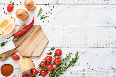 Baharatlı Pişirme Arkaplanı: biber, biberiye, paprika, limon, soğan, kuşkonmaz, zeytinyağı, domates, parmesan peyniri, ahşap zemin üzerinde pişirme tahtası ve peçete. Mutfak afişi. Üst görünüm.