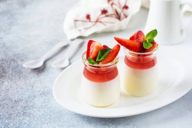 Vanilyalı panna cotta ve taze çilek, gri beton masa arkasında nane yaprakları. Böğürtlenli tatlı. Seçici odak.