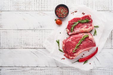 İki çiğ biftek New York biberiyesi ve eski beyaz ahşap arka planda parşömen kağıdına baharatlar. Üst Manzara. Model.