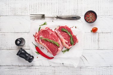 İki çiğ biftek New York biberiyesi ve eski beyaz ahşap arka planda parşömen kağıdına baharatlar. Üst Manzara. Model.