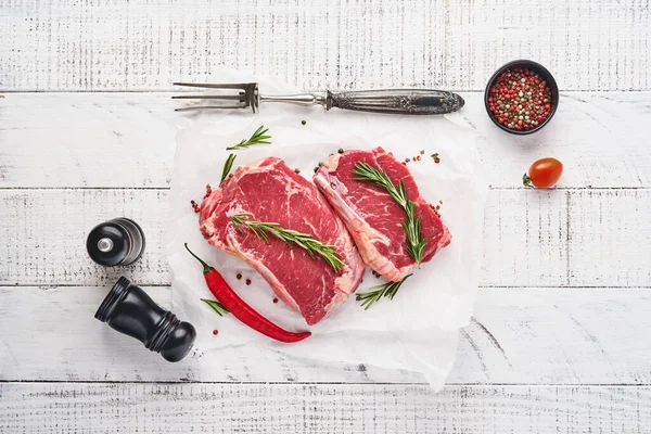 İki çiğ biftek New York biberiyesi ve eski beyaz ahşap arka planda parşömen kağıdına baharatlar. Üst Manzara. Model.