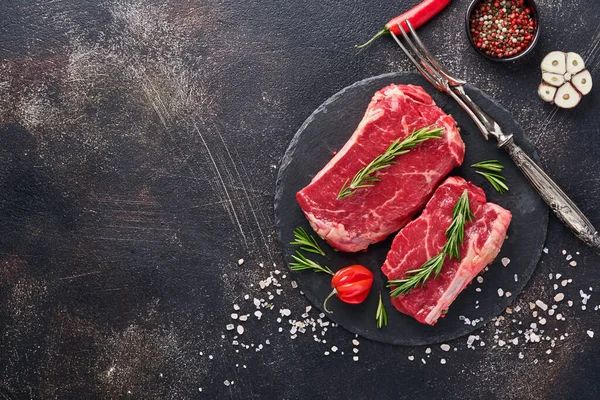 Biberiye ve baharatlı iki çiğ biftek. Siyah taş kesme masasının üstünde düz bir görünüm vardı..