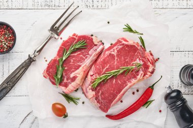 İki çiğ biftek New York biberiyesi ve eski beyaz ahşap arka planda parşömen kağıdına baharatlar. Üst Manzara. Model.