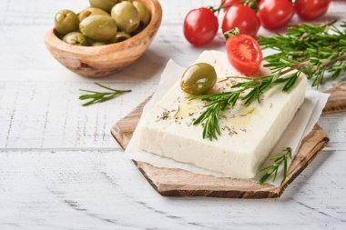 Biberiyeli peynirli feta, şifalı otlar, kiraz domatesleri, zeytin ve zeytinyağı beyaz ahşap arka planda tahta kesme tahtasında. Geleneksel Yunan ev yapımı peynir. Seçici odak.