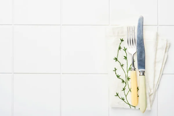 Food cooking background. Set of vintage fork, knife, napkin and pepper shaker on white ceramic tile background. Spring table setting. Top view. Copy space