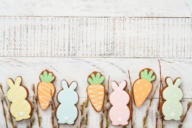 Pussy willows branches and Colorful easter gingerbread rabbit, eggs and chickens on white old wooden background. Festive Easter concept with copy space. Flat lay.