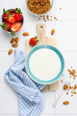 Kahvaltı gevreği ve beyaz masada taze çilek yapmak için malzemelerle dolu beyaz kasede Yunan yoğurdu. Üst görünüm