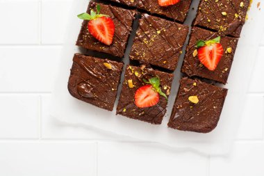 Fıstıklı çikolatalı kareler ve beyaz arkaplanda beyaz kağıt üzerinde çilek, üst manzara, yatay kompozisyon. Düz yiyecek.