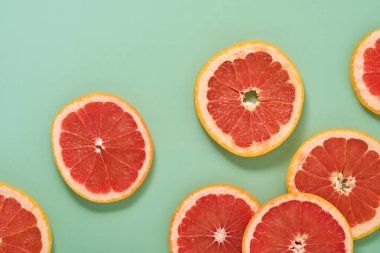 Greyfurt narenciye desenli kompozisyon. Meyve suyuyla yapılan greyfurt dilimleri, gölgeli yeşil bir zemine saçılmıştır. Yaz ya da bahar konsepti. Model yap. Üst görünüm.