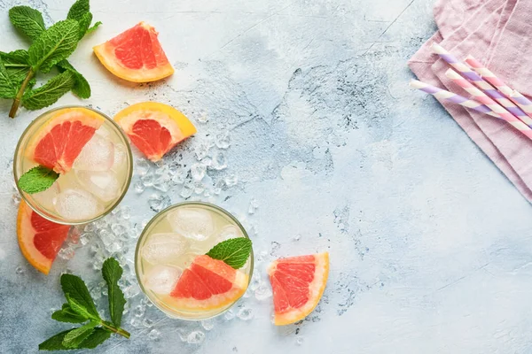 Lemonade drink made from grapefruit, soda water and mint leaves with ice on light blue slate, stone or concrete background. Healthy homemade lemonade or cocktail. Mock up. Top view.