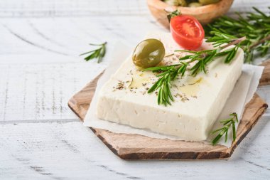 Biberiyeli peynirli feta, şifalı otlar, kiraz domatesleri, zeytin ve zeytinyağı beyaz ahşap arka planda tahta kesme tahtasında. Geleneksel Yunan ev yapımı peynir. Seçici odak.
