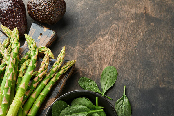Куча свежей зеленой органической спаржи шпинат, авокадо, куриные яйца и перец приправы на черном старом деревянном фоне, вид сверху. Кухонный фон с копировальным пространством. Mock up.