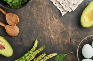 Bir demet taze yeşil organik kuşkonmaz ıspanak, avokado, tavuk yumurtası ve biber çeşnili siyah ahşap arka plan, üst manzara. Fotokopi alanı olan yemek pişirme arka planı. Model.