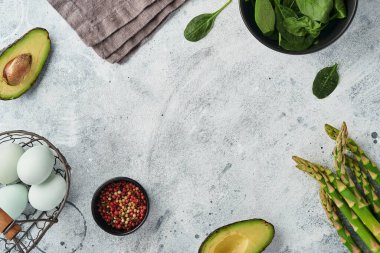 Bir demet taze yeşil organik kuşkonmaz ıspanak, avokado, tavuk yumurtası ve biber soslu gri arka plan, üst manzara. Fotokopi alanı olan yemek pişirme arka planı. Model.