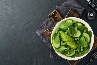Ispanaklı yeşil sebze salatası, avokado, yeşil bezelye ve zeytinyağı. Koyu levhada, taşta ya da betonda. Kopyalama alanı olan üst görünüm. Diyet konsepti için yeşil sebze.