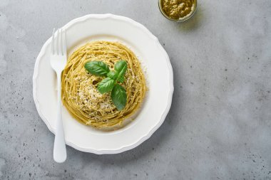 Pesto soslu makarna ve beyaz kasede taze fesleğen yaprağı. Gri arka plan. Model yap. Üst görünüm.