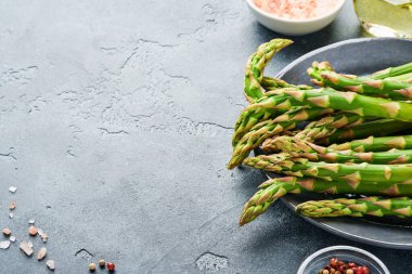 Kuşkonmaz. Taze yeşil kuşkonmaz sürüsü gri tahta masa arkasında pişmeye hazır. Üst görünüm kopyalama alanı.