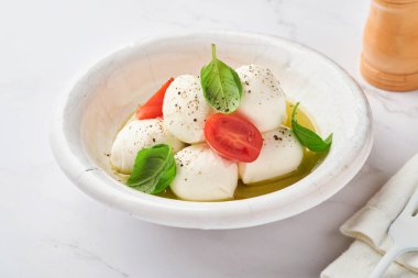 Caprese salatası. Beyaz seramik tabakta fesleğenli ve kirazlı Mozzarella peyniri ve kayrak taşı zemin üzerinde domates vişnesi, kopyalama alanı. Model.