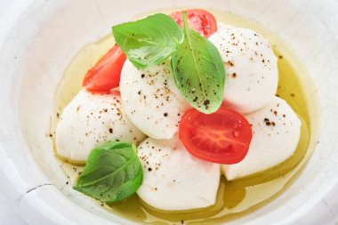 Caprese salatası. Beyaz seramik tabakta fesleğenli ve kirazlı Mozzarella peyniri ve kayrak taşı zemin üzerinde domates vişnesi, kopyalama alanı. Model.