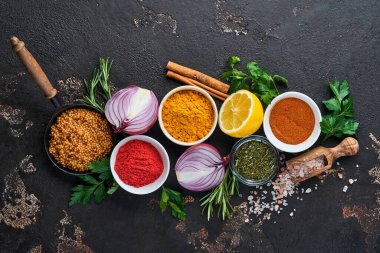 Siyah taştan bir arka planda Hint baharatları ve otları. Bir kaşıkta zerdeçal, dereotu, paprika, tarçın, safran, fesleğen ve biberiye. Üst Manzara. Model.