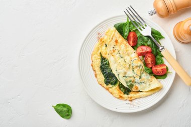 Ispanaklı omlet, kiraz domatesli ve biberli omlet beyaz bir tabakta, beyaz arka planda. Üst görünüm.