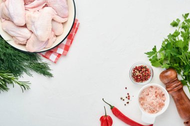 Beyaz bir kasede çiğ tavuk kanadı. Baharat ve malzemelerle hafif kayrak, taş ya da beton arka planda yemek pişirmek için. Kopyalama alanı olan üst görünüm. Model.