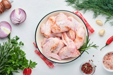 Beyaz bir kasede çiğ tavuk kanadı. Baharat ve malzemelerle hafif kayrak, taş ya da beton arka planda yemek pişirmek için. Kopyalama alanı olan üst görünüm. Model.