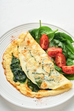 Ispanaklı omlet, kiraz domatesli ve biberli omlet beyaz bir tabakta, beyaz arka planda. Üst görünüm.